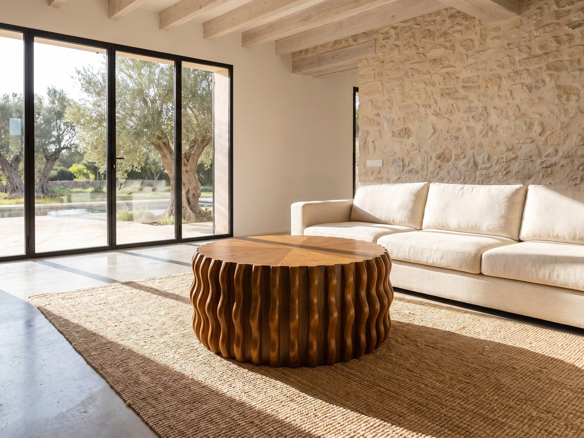 Rivoli 30-Inch Round Carved Wood Drum Coffee Table on a jute rug in front of a linen sofa in a poolside villa