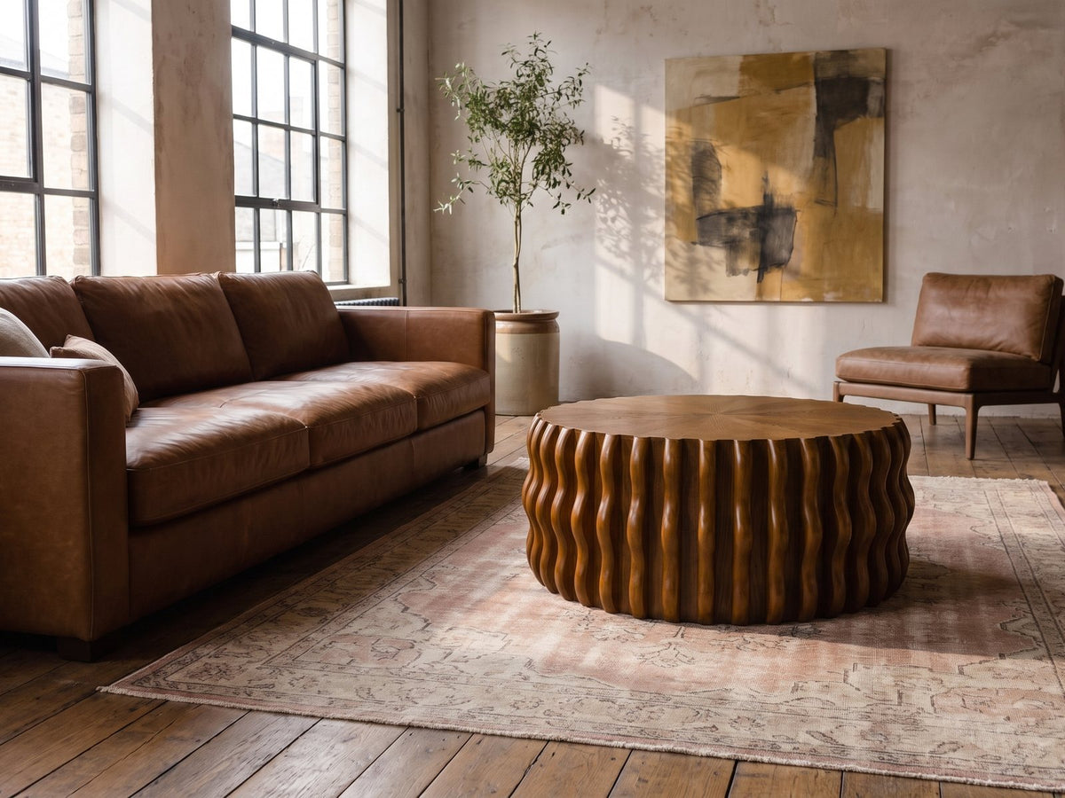 Rivoli 30-Inch Round Carved Wood Drum Coffee Table on a vintage rug in front of a leather sofa in an industrial loft