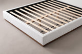 The slat deck at the foot corner of the Roccascalegna bed: pale wooden slats on a centre support inside the white boucle rails, above the walnut-tone plinth