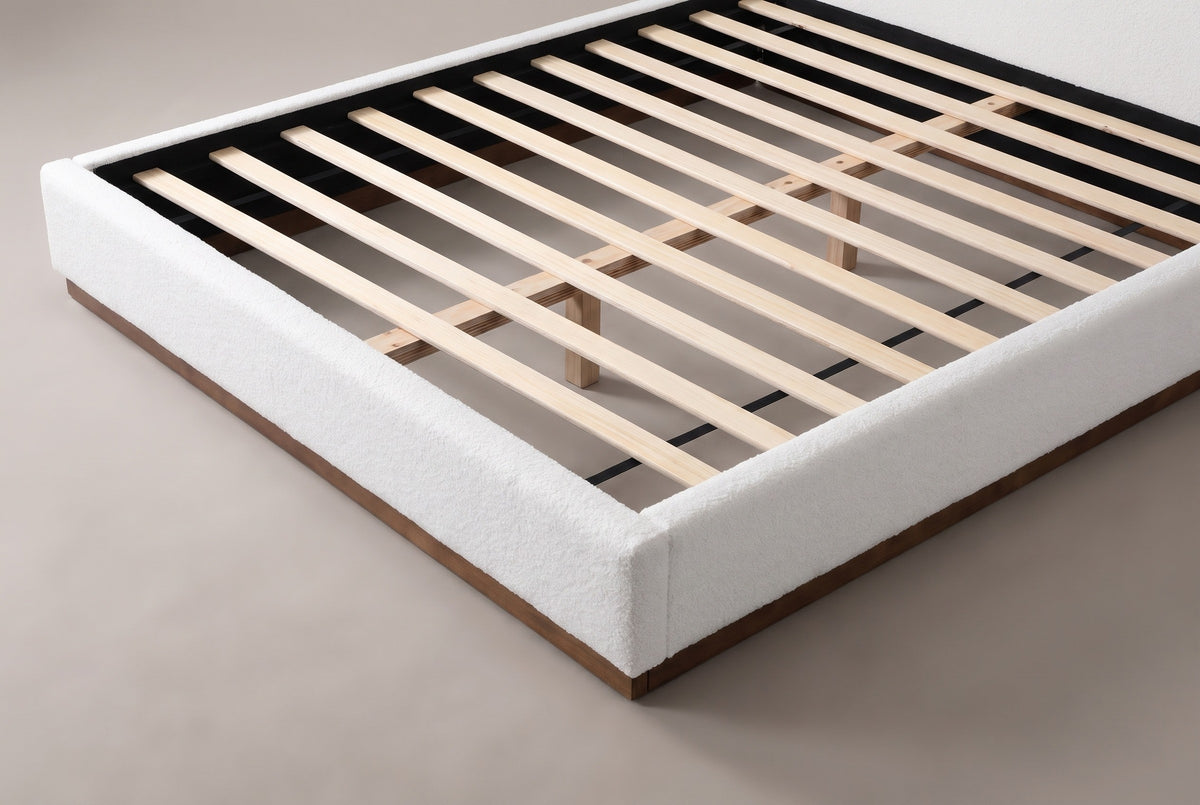 The slat deck at the foot corner of the Roccascalegna bed: pale wooden slats on a centre support inside the white boucle rails, above the walnut-tone plinth
