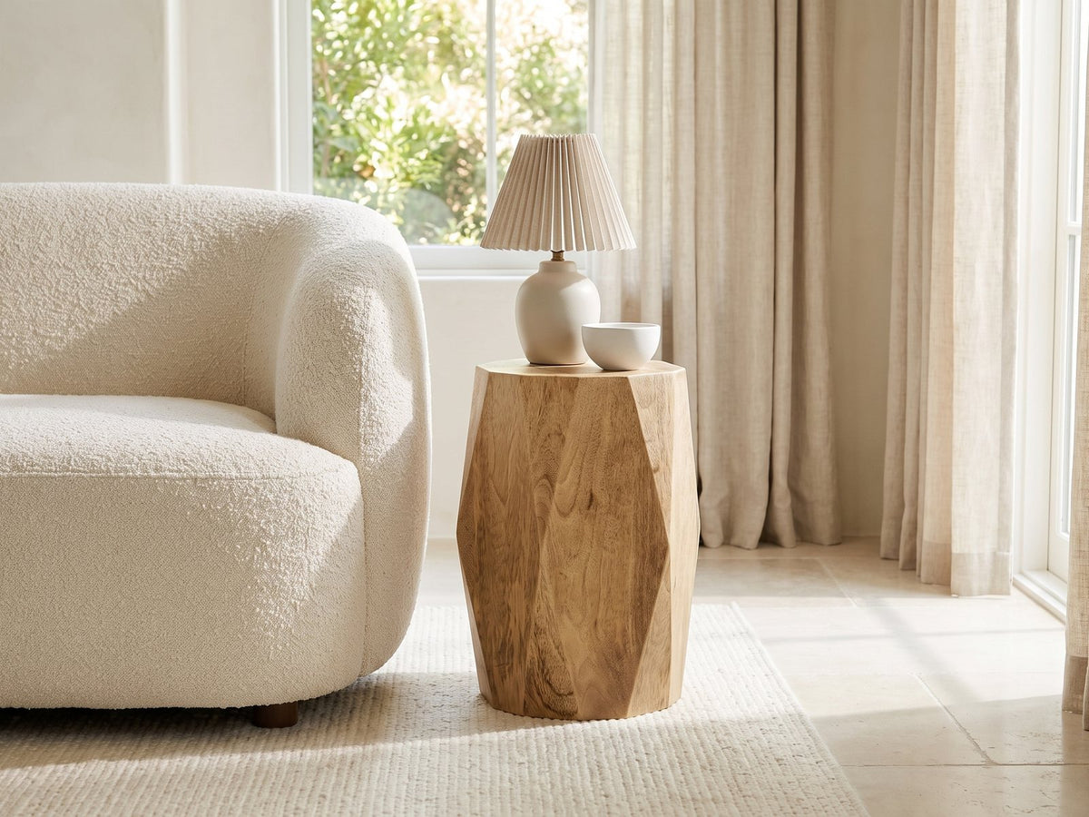 Rotondella Faceted Mango Drum Side Table with a lamp and a ceramic bowl beside a cream boucle armchair in a bright plaster room