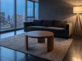 Rovereto Brown Ash Veneer Round Coffee Table on a wool rug in front of a velvet sofa in a city penthouse at blue hour