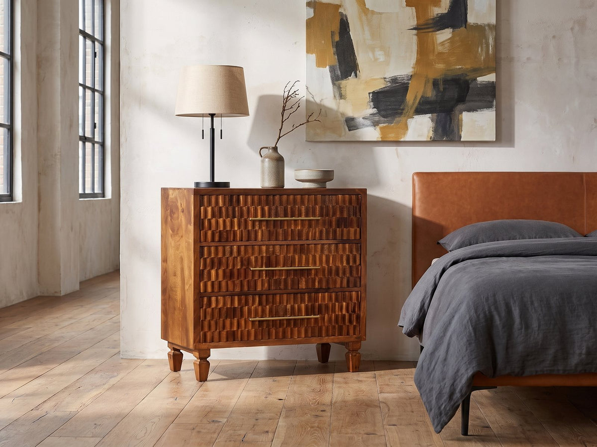 Rovigo 33-Inch Chestnut Carved Mango 3-Drawer Chest against a plaster wall in an industrial loft bedroom