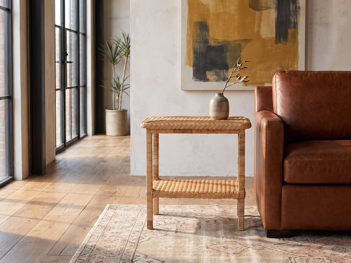 Rutigliano Braided Rattan Two-Tier Side Table beside a cognac leather armchair in an industrial loft