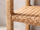 Close-up of the Rutigliano Braided Rattan Two-Tier Side Table: the braided rattan shelf edge and a rattan-wrapped leg