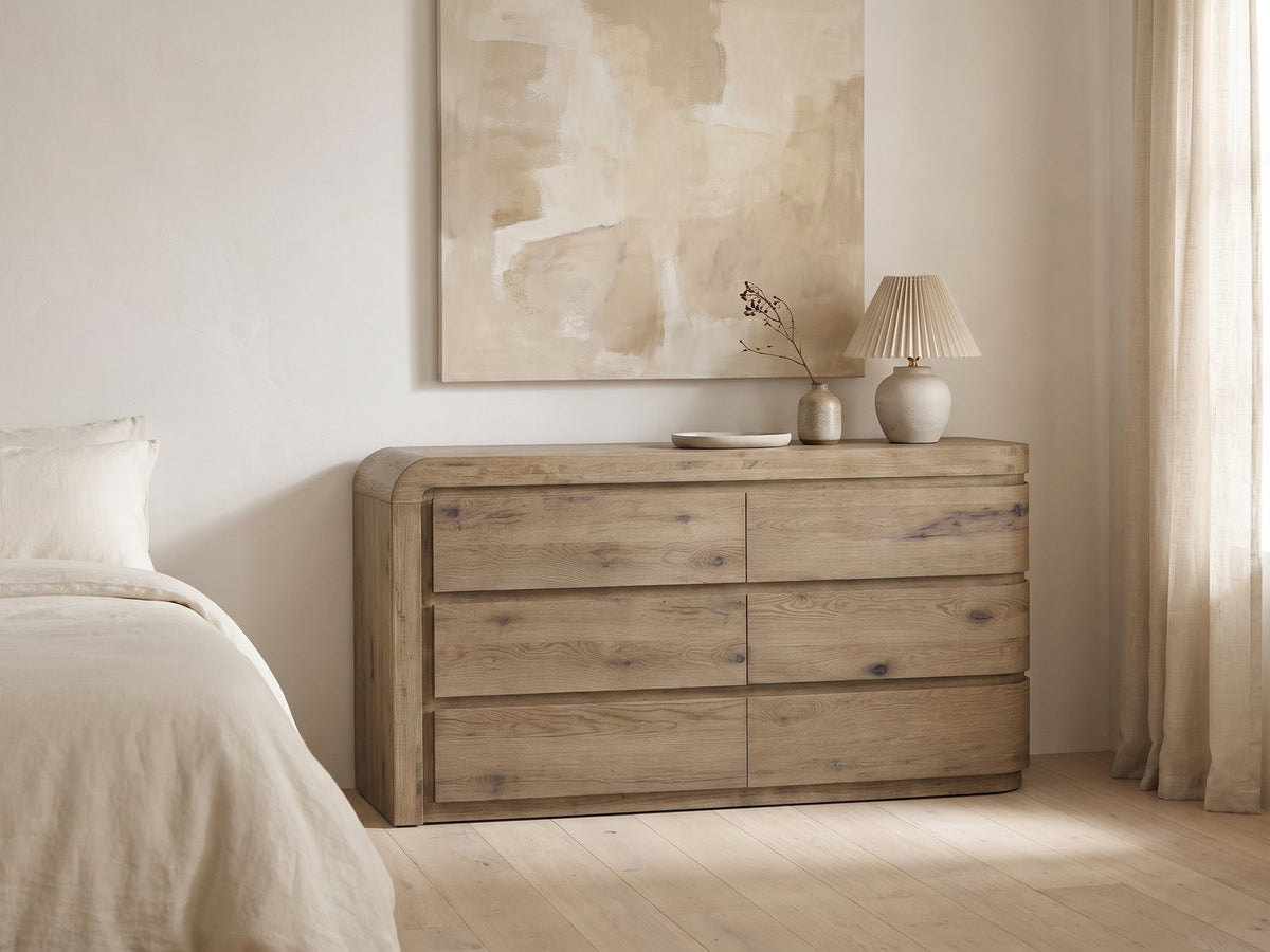 Sacile 70-Inch Weathered Natural Oak 6-Drawer Dresser against a plaster wall under an abstract canvas in a bright bedroom