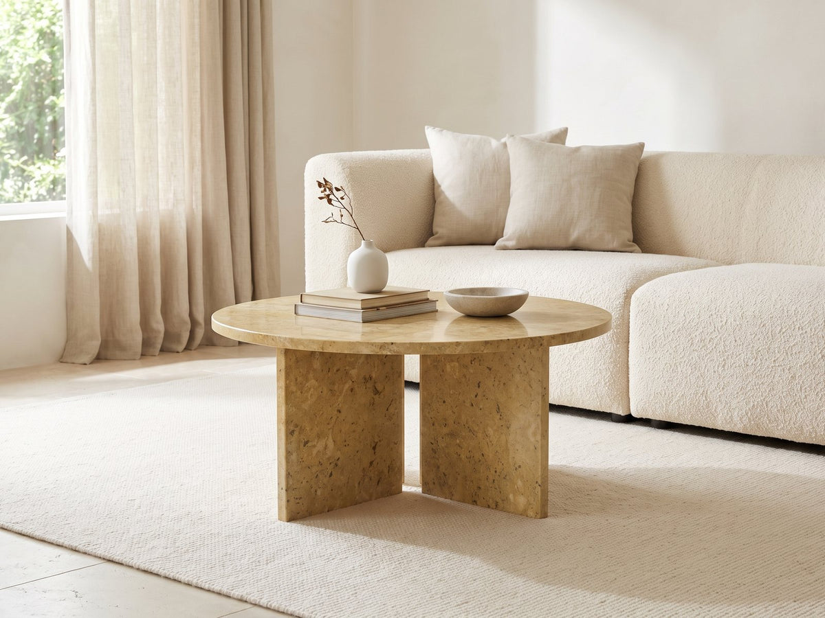Salina Gold Beige Marble Coffee Table styled with books, a vase and a stone bowl in front of a cream sofa in a bright plaster room
