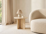 Salina Gold Beige Marble Round Side Table with a lamp and a ceramic bowl beside a cream boucle armchair in a bright plaster room