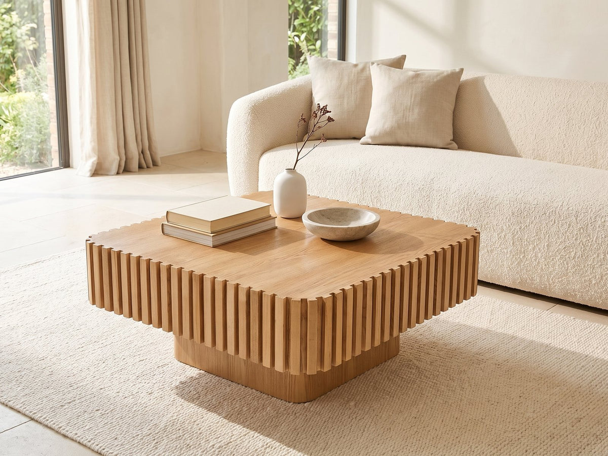 Saluzzo 35-Inch Square Slatted Natural Wood Veneer Coffee Table styled with books, a vase and a stone bowl in front of a cream sofa in a bright plaster room
