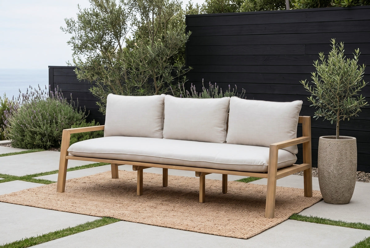 The Sambuca acacia outdoor sofa on a jute rug on a Laguna Beach concrete terrace, a black-stained cedar fence, olive trees and lavender behind (rug and planter not included)