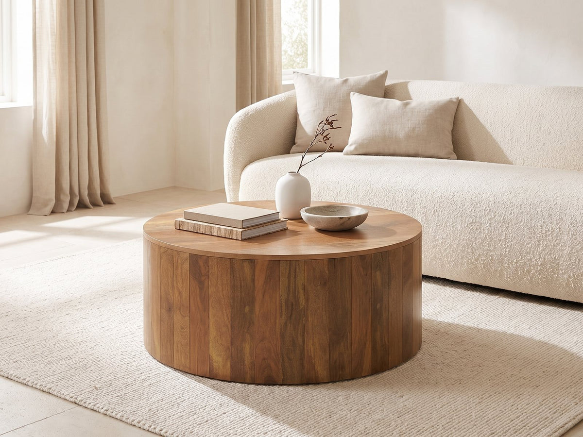 Sansepolcro Natural Mango Drum Coffee Table styled with books, a vase and a stone bowl in front of a cream sofa in a bright plaster room
