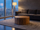 Sansepolcro Natural Mango Drum Coffee Table on a wool rug in front of a velvet sofa in a city penthouse at blue hour