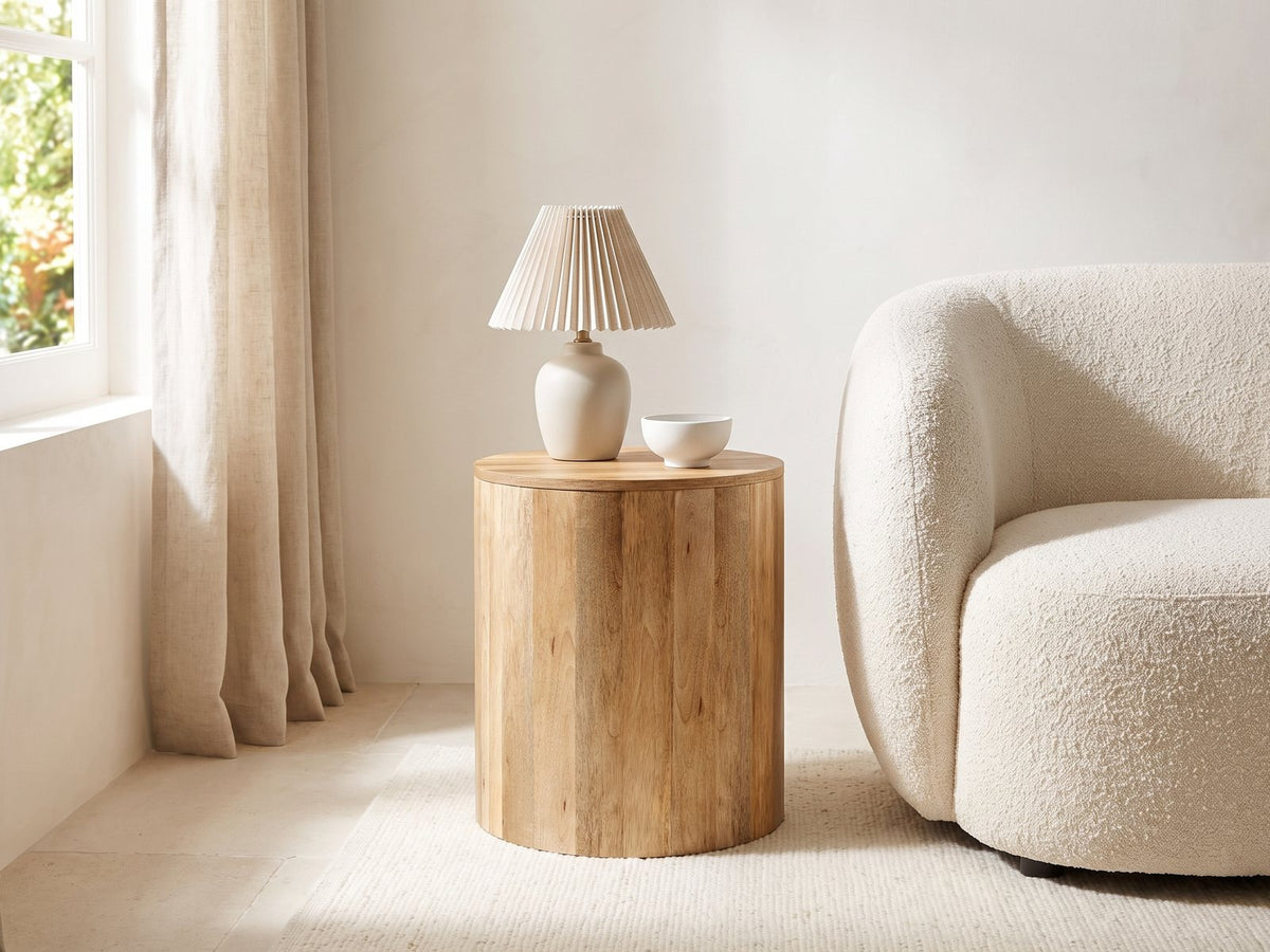 Sansepolcro Natural Mango Drum Side Table with a lamp and a ceramic bowl beside a cream boucle armchair in a bright plaster room