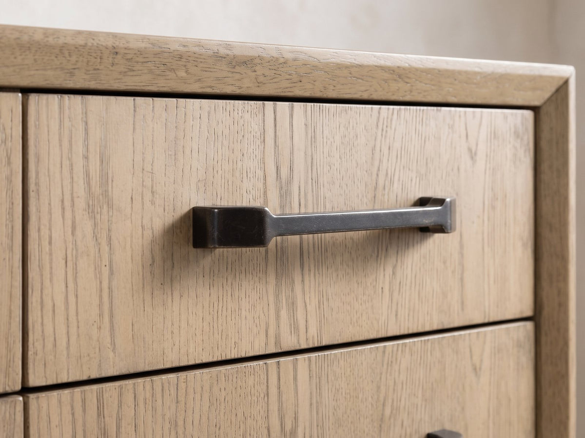 Close-up of the Sappada 54-Inch Caramel Oak and Cocoa 12-Drawer Chest: a dark bronze bar pull on a drawer front in pale caramel oak