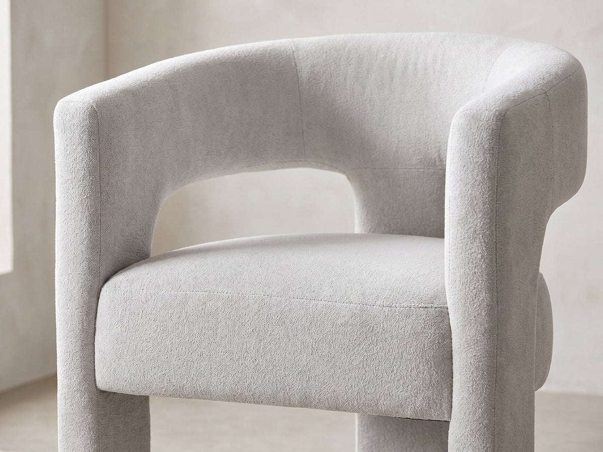 Close-up of the Saracena 54-Inch Round Ebony Oak Dining Set with 4 Boucle Chairs: the curved back and arms of a chair in light grey boucle