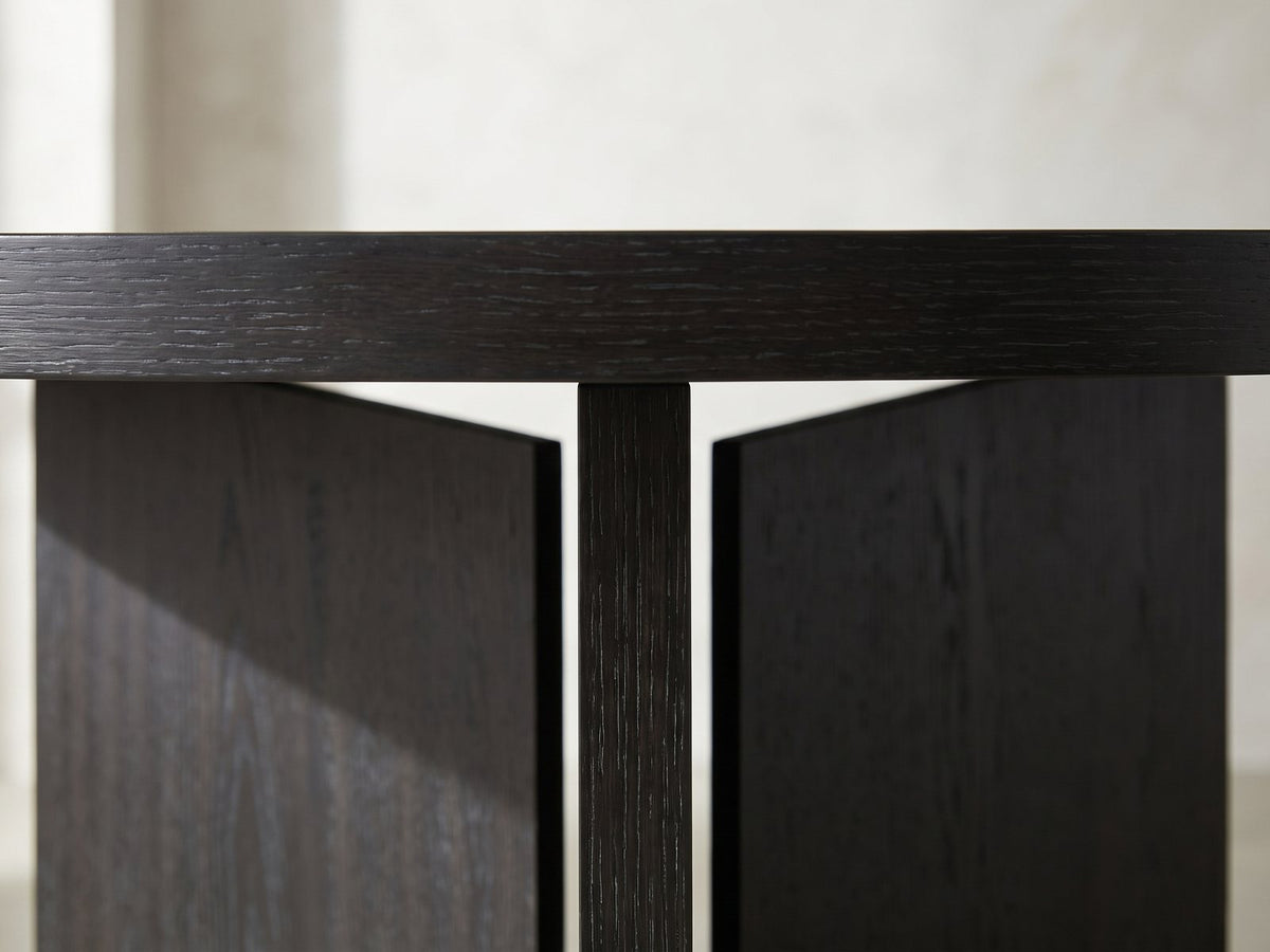 Close-up of the Saracena 54-Inch Round Ebony Oak Dining Set with 4 Boucle Chairs: the thick edge of the ebony oak top over the slab blades of the pedestal