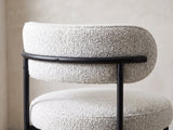 Close-up of the Savelli 47-Inch Round Black Oak Pedestal Dining Set with 4 Boucle Chairs: the curved boucle back band and black metal frame of a chair