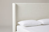 One side of the Scanno headboard: a tall flat ivory canvas panel with a slim rounded wing running down beside it, above a white mattress with two white pillows