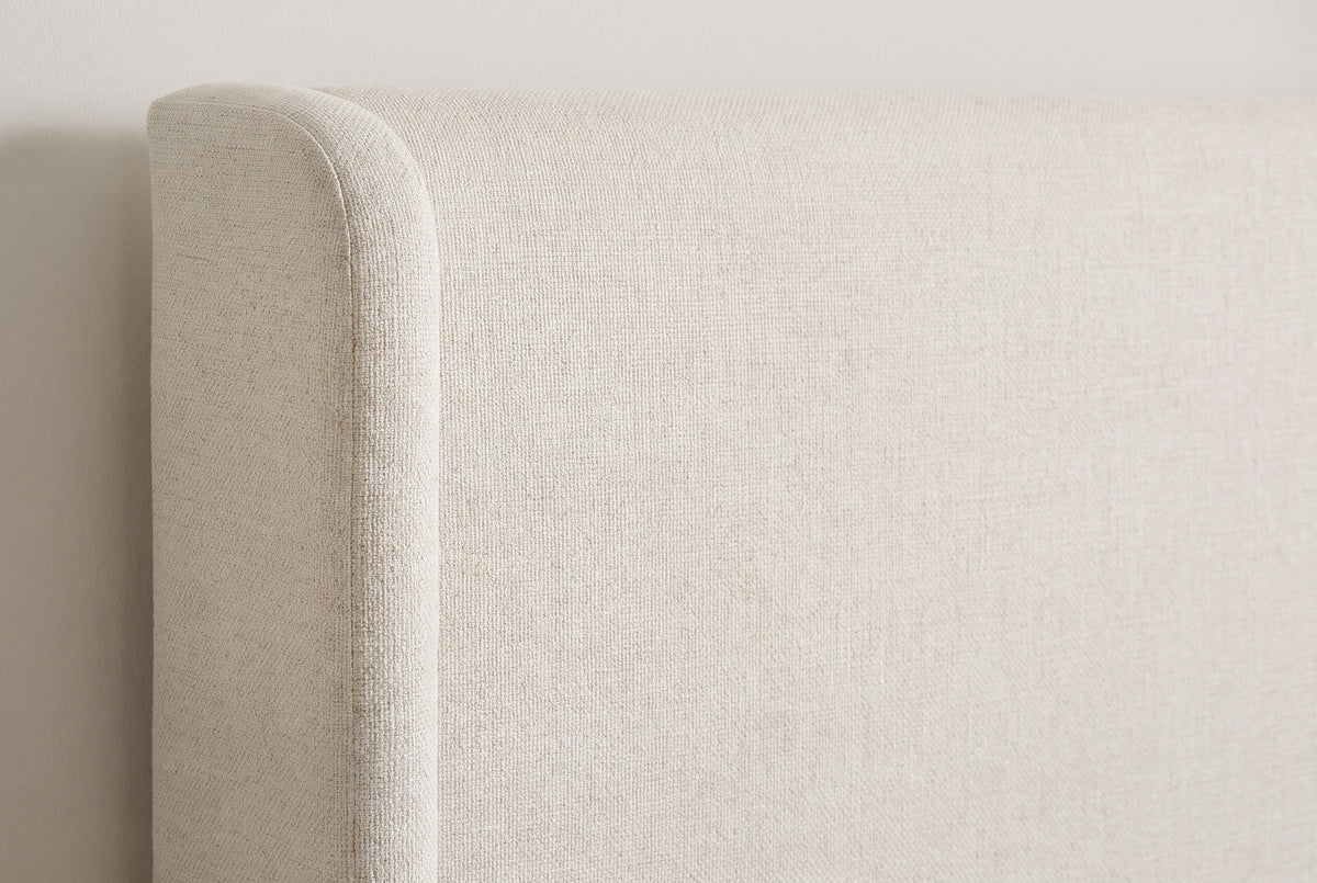 Close-up of the Scanno headboard in ivory canvas: the rounded top of a slim wing beside the flat panel