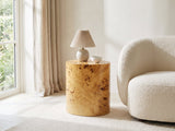 Scapoli Burl Veneer Oval Pillar Side Table with a lamp and a ceramic bowl beside a cream boucle armchair in a bright plaster room