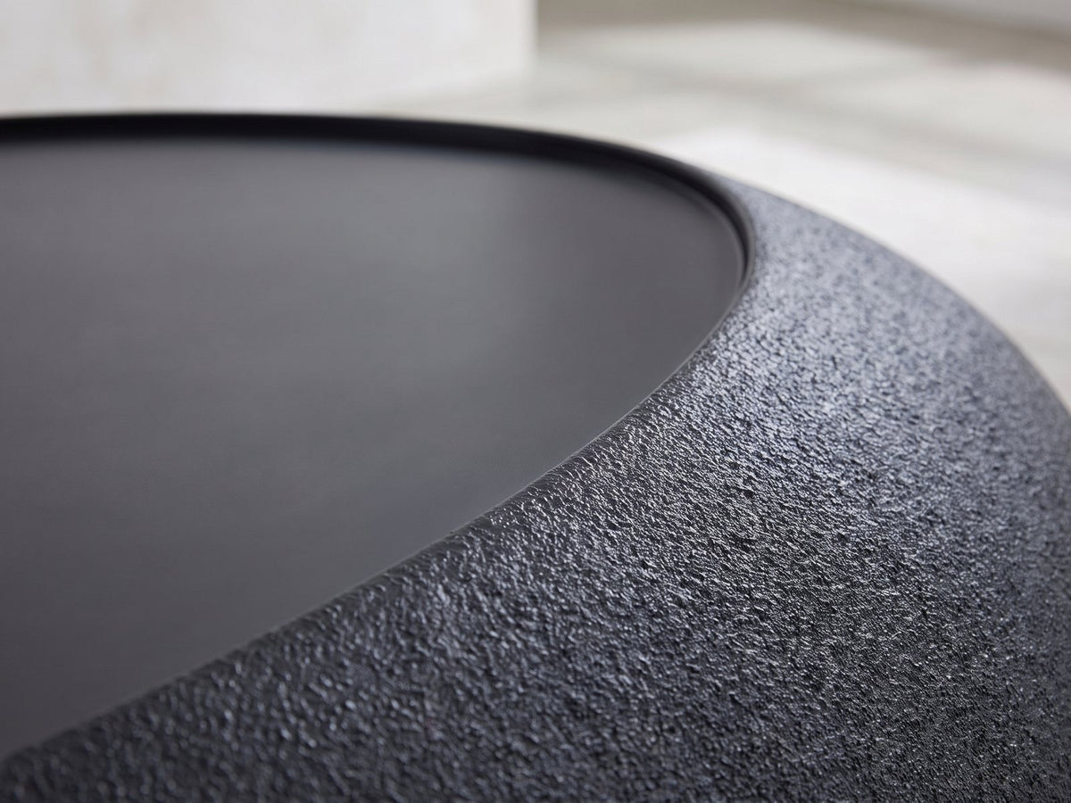 Close-up of the Scicli Black Fiberglass Pebble Coffee Table: the textured black rim around the smooth charcoal top