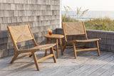 Two Scopello acacia and wicker lounge chairs on a grey weathered deck beside a Carolina coast cedar-shingle wall, with sea oats and the ocean beyond (side table and drink not included)
