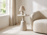 Segesta Whitewashed Mango Pedestal Side Table with a lamp and a ceramic bowl beside a cream boucle armchair in a bright plaster room