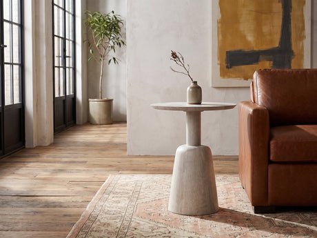 Segesta Whitewashed Mango Pedestal Side Table with a stoneware vase beside a cognac leather armchair in an industrial loft