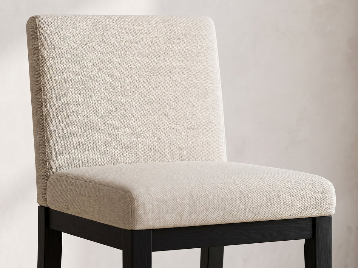 Close-up of the Sellia 59-Inch Round Ebony Cone Pedestal Dining Set with 4 Chairs: the beige upholstered back and seat of a chair on its black wood base