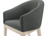Close-up of the Seminara 80-Inch Oval Fluted Pedestal Dining Set with 6 Chairs: the curved barrel back and low arms of a chair in charcoal-grey fabric on pale wood legs