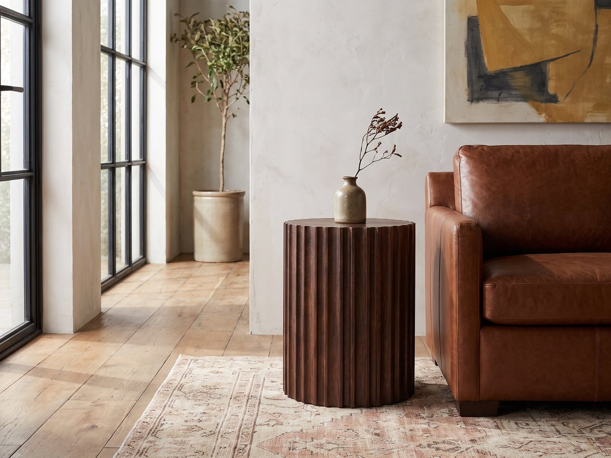 Senise Walnut Mango Fluted Drum Side Table beside a leather sofa in an industrial loft