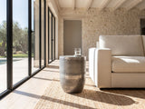 Sepino Antique Silver Metal Drum Side Table beside a linen sofa in a poolside villa