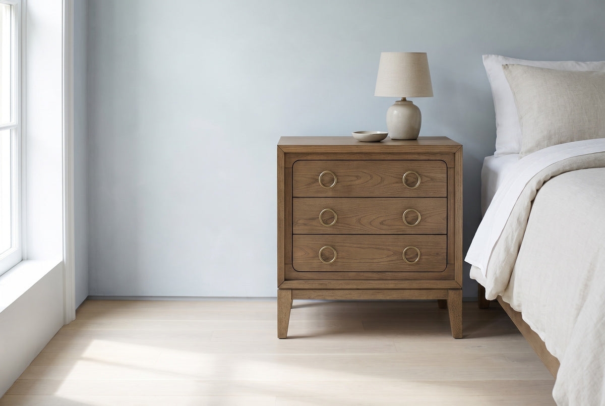 Serramanna latte elm three-drawer nightstand with a ceramic lamp beside a bed in a Brooklyn bedroom with a pale blue-grey limewash wall