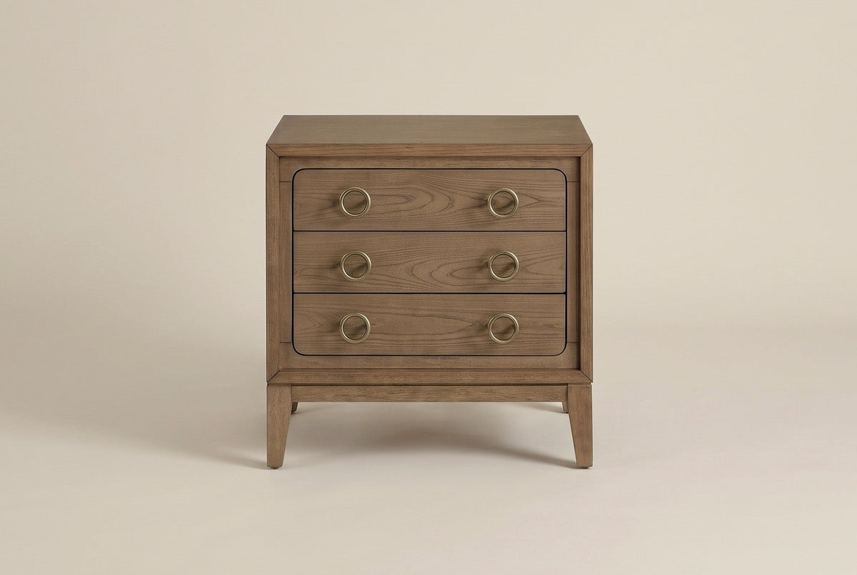 The Serramanna nightstand in latte elm with six antique-brass ring pulls, front view on a light studio backdrop