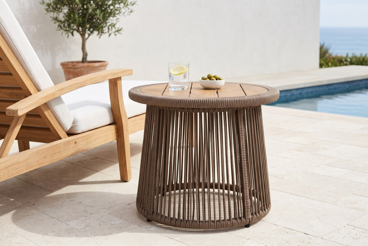 Siculiana dark beige rope and acacia side table with sparkling water and a bowl of olives beside a teak lounge chair on a limestone pool terrace in La Jolla, a white limewashed wall behind (chair and decor not included)