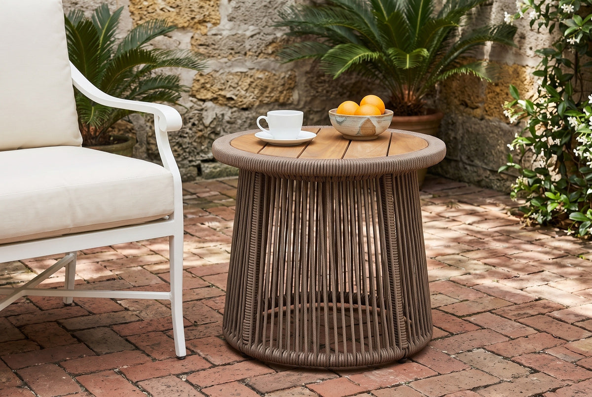 Siculiana rope side table with a coffee cup and a bowl of oranges beside a white armchair in a St. Augustine courtyard, a coquina stone wall and red brick pavers (chair and decor not included)