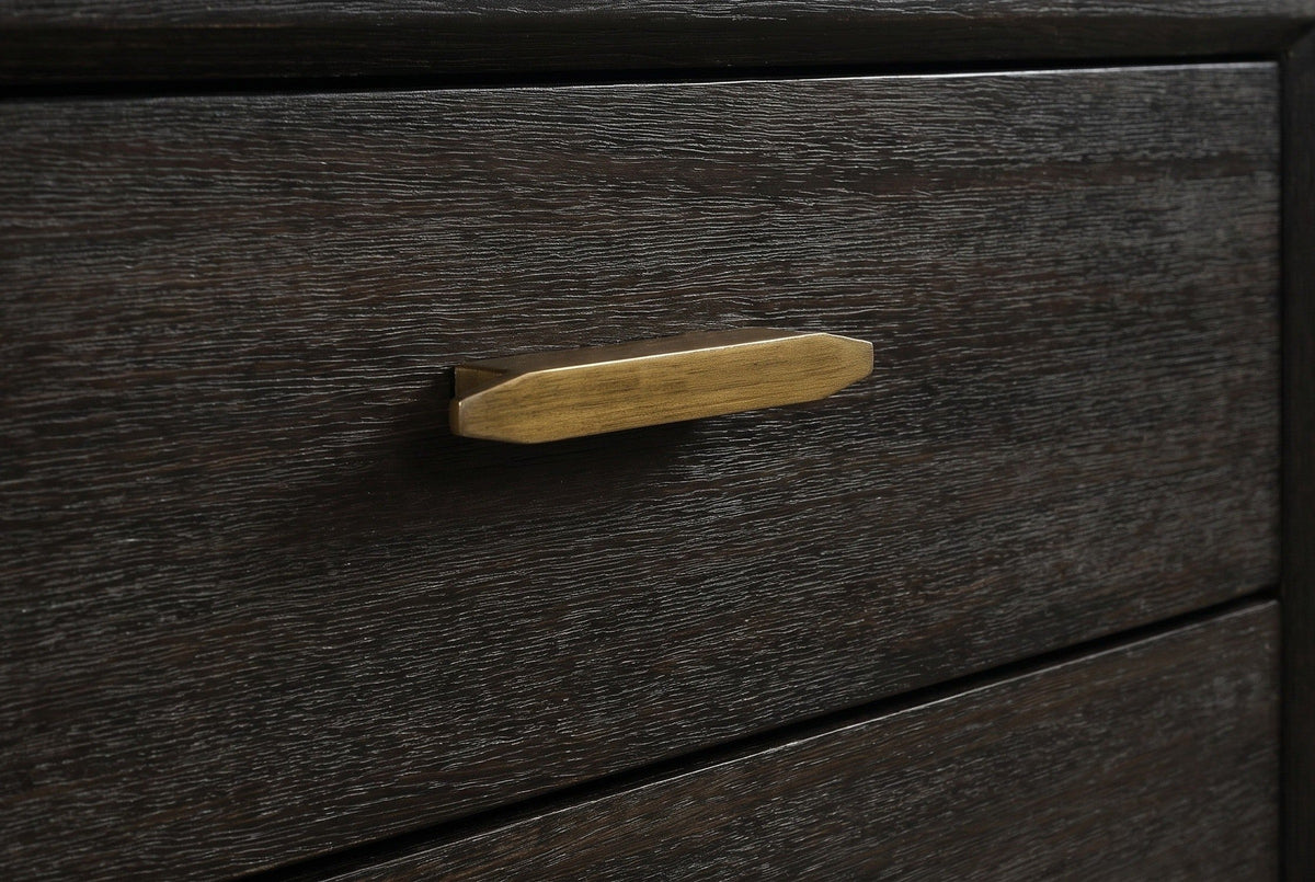 The upper drawer of the Siniscola nightstand: a slim antique-brass bar pull with faceted ends on dark wire-brushed acacia
