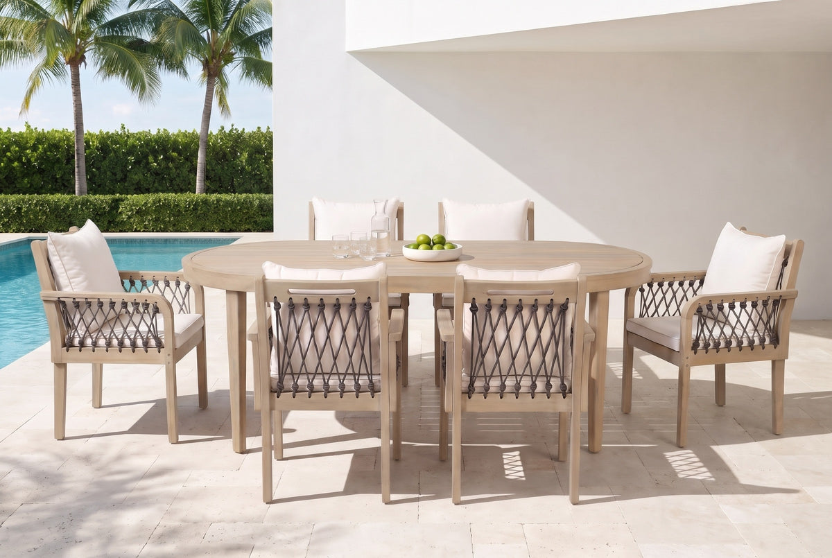 Siracusa light teak oval dining set with six dark gray rope armchairs on a travertine pool terrace at a white stucco house in Naples, Florida, palms and a hedge behind (tableware not included)