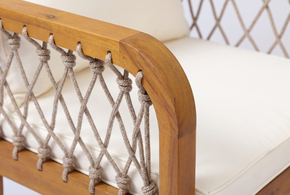Close-up of a Siracusa armchair arm: honey teak acacia curving down into the front leg, oatmeal rope knotted through the rail