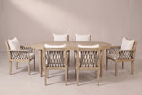 The Siracusa 7-piece dining set in light teak: an acacia oval table and six armchairs with dark gray rope and ivory cushions on a light studio backdrop