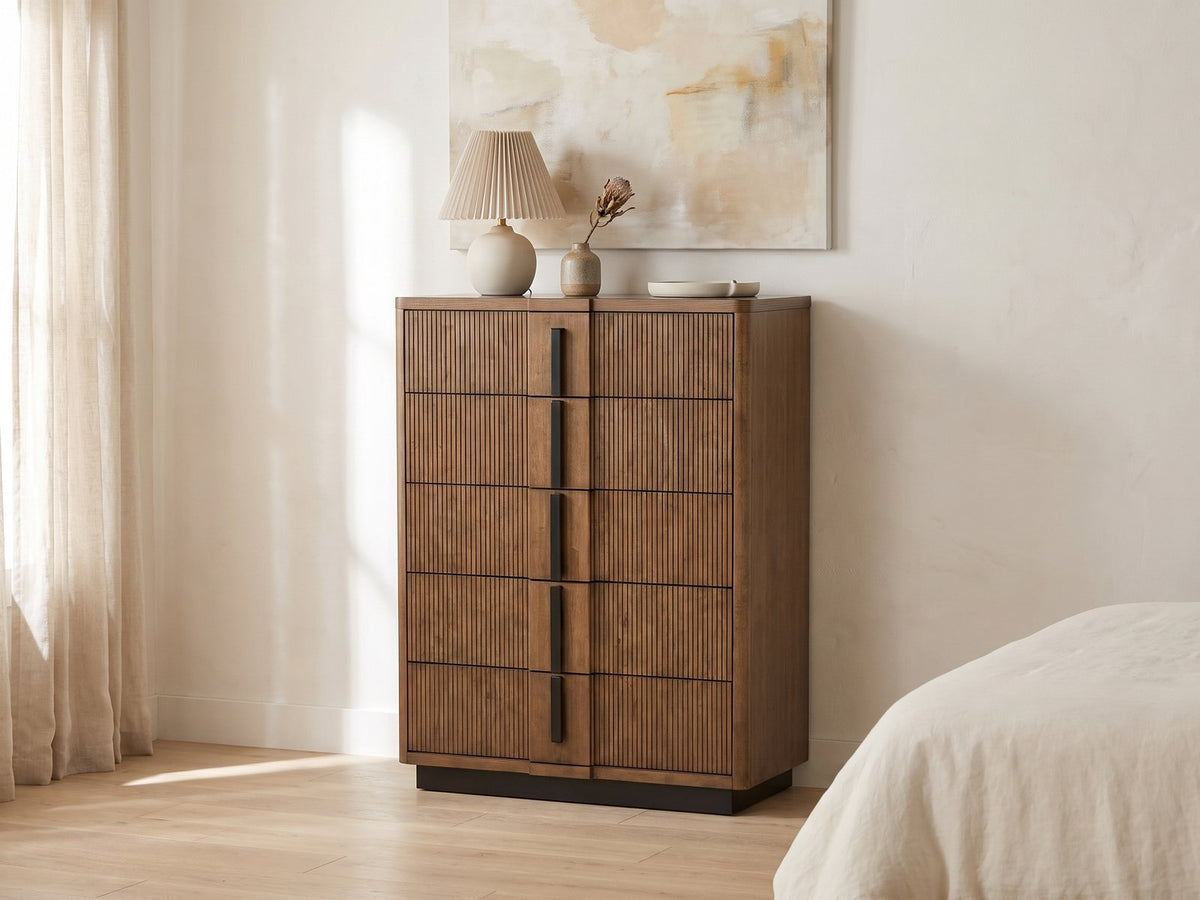 Soave 40-Inch Ash Brown Reeded 5-Drawer Chest against a plaster wall under an abstract canvas in a bright bedroom