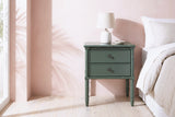 Sorgono green faux-bamboo nightstand with a ceramic lamp beside a bed in a Palm Beach bedroom with a blush pink plaster wall