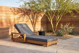Sortino acacia chaise lounge in a Tucson courtyard at golden hour, a rammed-earth wall in rust and ochre bands and a palo verde tree behind (side table not included)