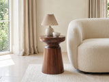 Specchia Brown Mango Cone Pedestal Side Table with a lamp and a ceramic bowl beside a cream boucle armchair in a bright plaster room
