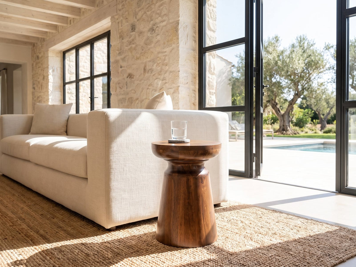 Specchia Brown Mango Cone Pedestal Side Table beside a linen sofa in a poolside villa