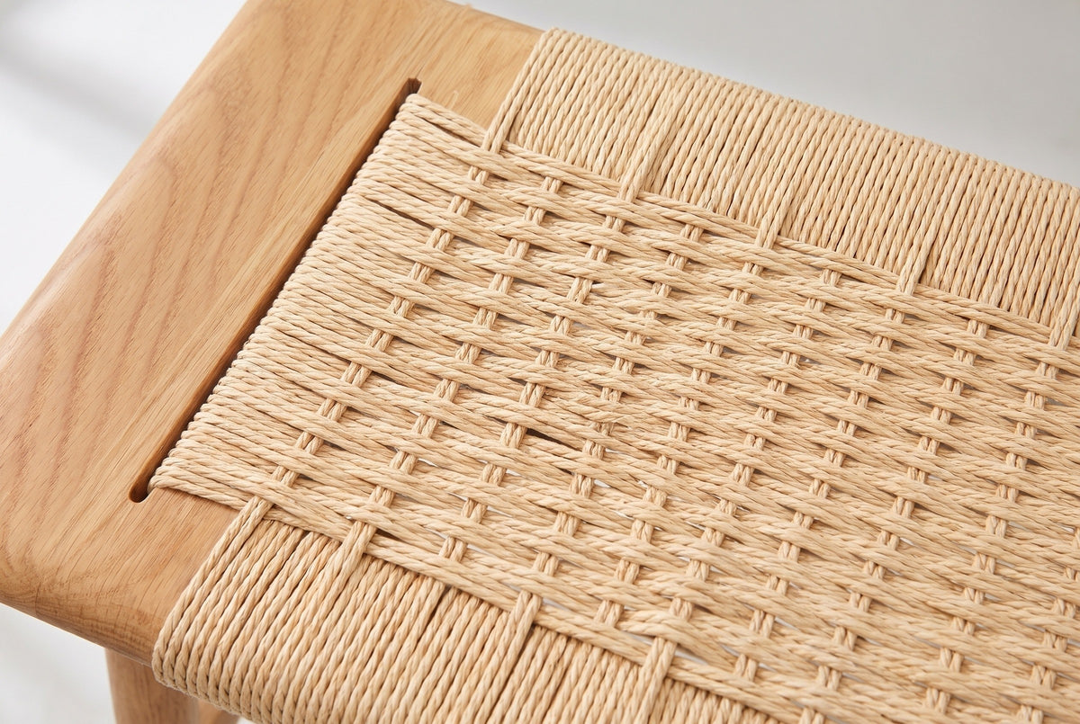 Close-up of the woven paper cord seat of the Sperlonga bench beside a block of bare oak: pale wheat twisted cords passing over and under pairs of crosswise cords