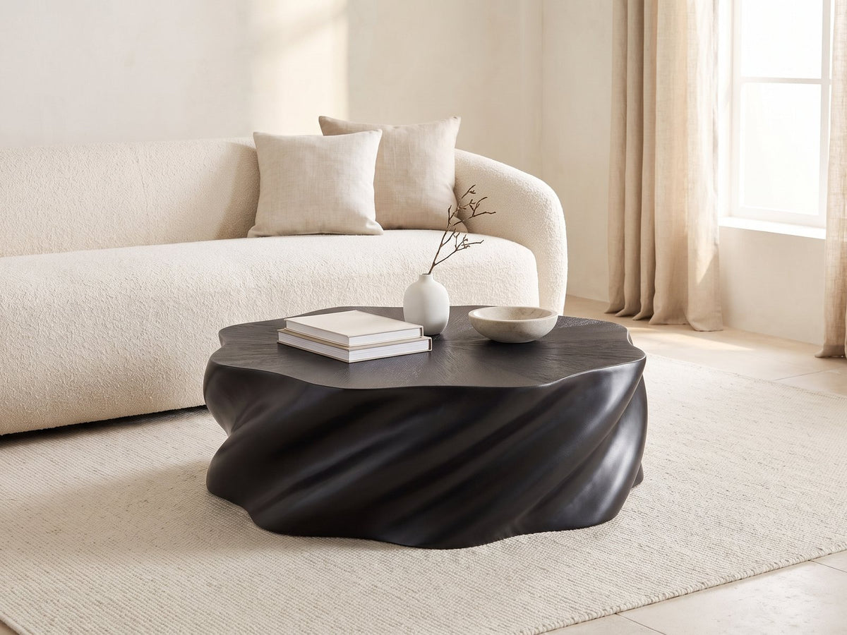 Spilimbergo Black Fiberglass Twisted Petal Coffee Table styled with books, a vase and a stone bowl in front of a cream sofa in a bright plaster room