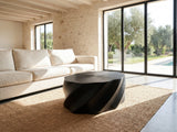 Spilimbergo Black Fiberglass Twisted Petal Coffee Table seen from the side, on a jute rug in front of a linen sofa in a poolside villa