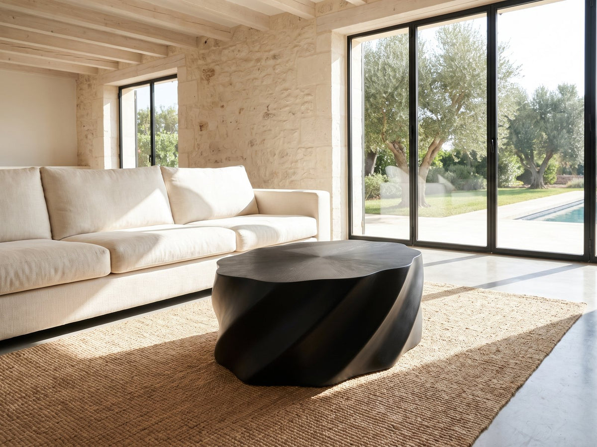 Spilimbergo Black Fiberglass Twisted Petal Coffee Table seen from the side, on a jute rug in front of a linen sofa in a poolside villa