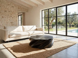 Spilimbergo Black Fiberglass Twisted Petal Coffee Table on a jute rug in front of a linen sofa in a poolside villa